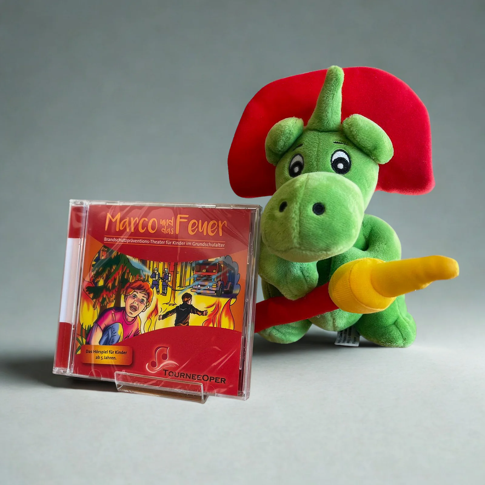 Abbildung der "Marco und das Feuer" Hörspiel CD links neben der Plüschfigur "Grisu" , einem kleinen Feuerwehr-Drachen